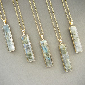 Puede incluir: Cinco collares de oro con colgantes de piedra labradorita. Cada colgante tiene forma de barra rectangular con un acabado liso y pulido. Las piedras son una mezcla de gris, azul y verde.