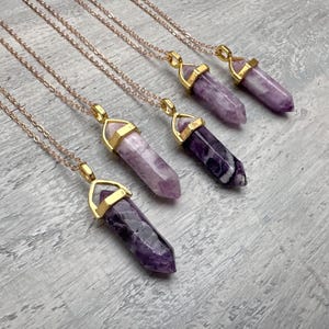 Puede incluir: Cuatro collares con colgantes de cristal de amatista morada tallados en forma hexagonal puntiaguda. Cada cristal est&aacute; asegurado en una tapa de metal dorado y suspendido de una delicada cadena dorada. Las piedras var&iacute;an de lila a violeta.
