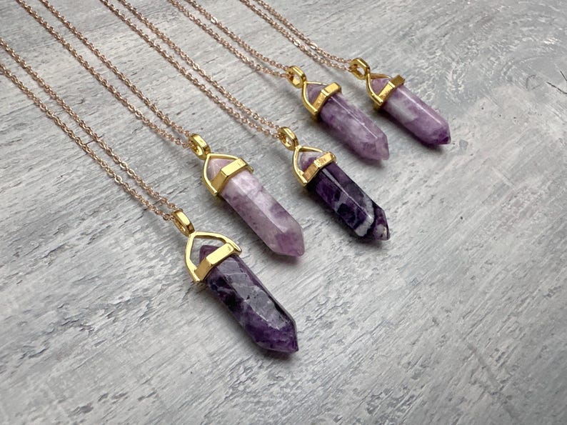 Puede incluir: Cuatro collares con colgantes de cristal de amatista morada tallados en forma hexagonal puntiaguda. Cada cristal est&aacute; asegurado en una tapa de metal dorado y suspendido de una delicada cadena dorada. Las piedras var&iacute;an de lila a violeta.
