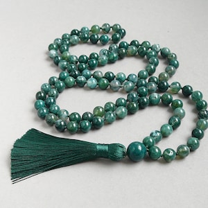 May include: A green agate mala necklace with a green tassel. The necklace is made of round beads and is approximately 108 beads long.