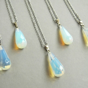 May include: Five silver necklaces with teardrop-shaped opal pendants. The opals are iridescent and have a light blue and white color.