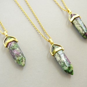 May include: Three gold chain necklaces with green, pink, and white gemstone pendants. Each pendant is a pointed crystal shape with a gold setting.