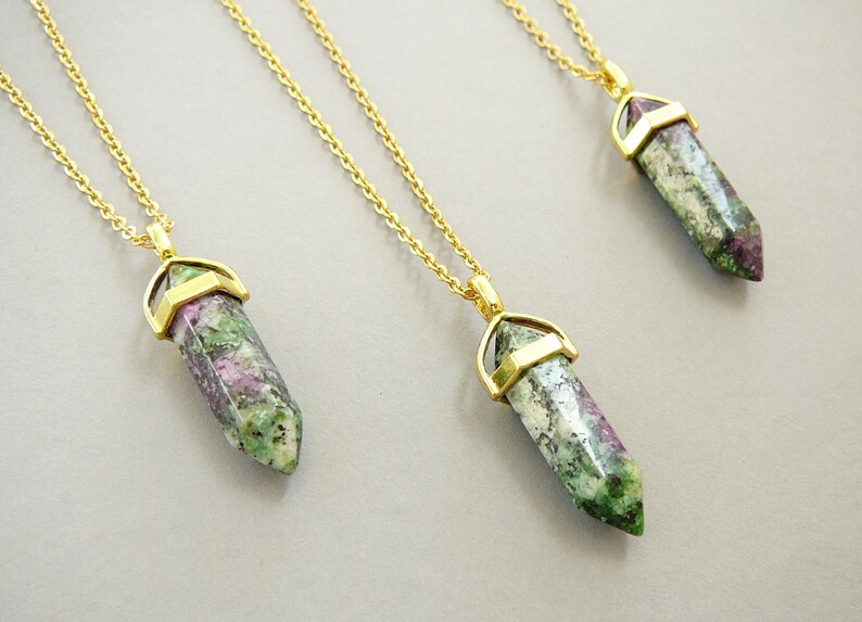 May include: Three gold chain necklaces with green, pink, and white gemstone pendants. Each pendant is a pointed crystal shape with a gold setting.