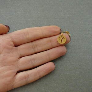 May include: A gold necklace with a small round pendant featuring the zodiac symbol for Aries.