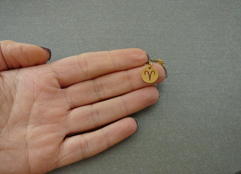 May include: A gold necklace with a small round pendant featuring the zodiac symbol for Aries.