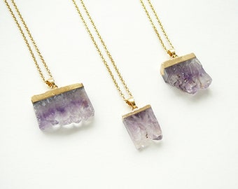 Könnte beinhalten: Drei goldene Kettenhalsbänder mit Amethyst-Kristallanhängern. Die Kristalle sind roh und haben eine natürliche, unregelmäßige Form. Die goldenen Ketten sind zart und haben ein schlichtes Design.