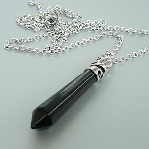 May include: A silver chain necklace with a black crystal point pendant. The pendant has a silver filigree design around the top.