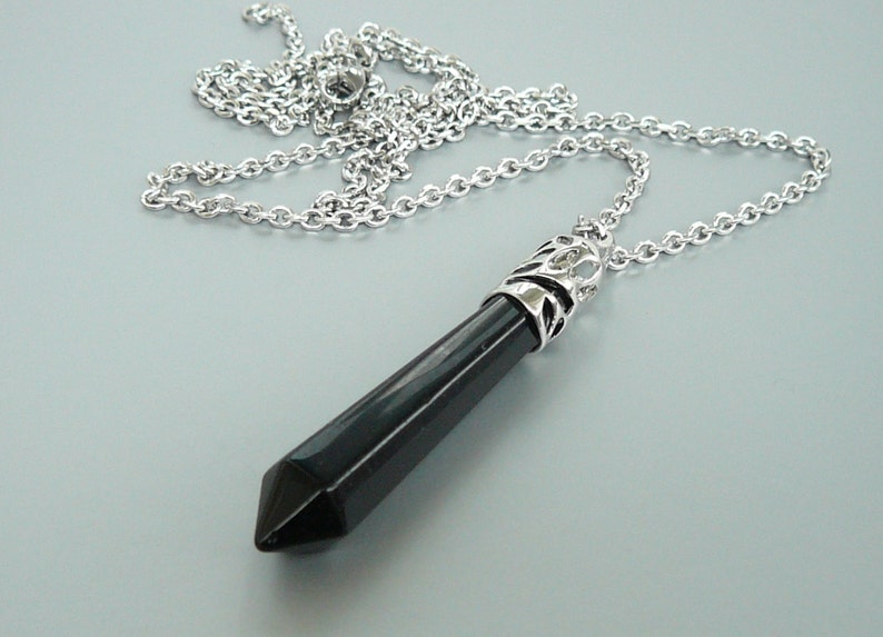May include: A silver chain necklace with a black crystal point pendant. The pendant has a silver filigree design around the top.