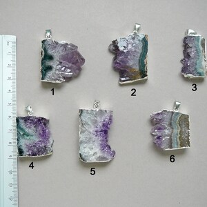 Pode incluir: Seis pingentes de cristal de ametista com ganchos de metal prateado, numerados de um a seis, dispostos ao lado de uma r&eacute;gua com medidas em cent&iacute;metros. Cada pingente apresenta forma&ccedil;&otilde;es de cristal roxo bruto com faixas minerais.