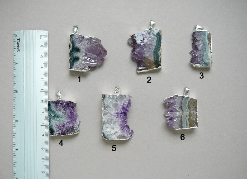 Pode incluir: Seis pingentes de cristal de ametista com ganchos de metal prateado, numerados de um a seis, dispostos ao lado de uma r&eacute;gua com medidas em cent&iacute;metros. Cada pingente apresenta forma&ccedil;&otilde;es de cristal roxo bruto com faixas minerais.