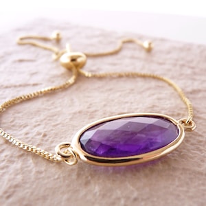 May include: A gold chain bracelet with an adjustable sliding clasp. The bracelet features a large, oval-shaped amethyst gemstone.