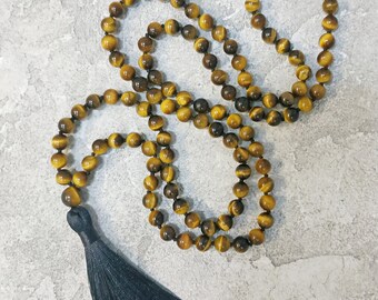 May include: A brown and gold tiger's eye beaded necklace with a black tassel.