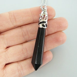 May include: A black gemstone pendant with a silver filigree design. The pendant is shaped like a long, pointed teardrop and hangs from a silver chain.