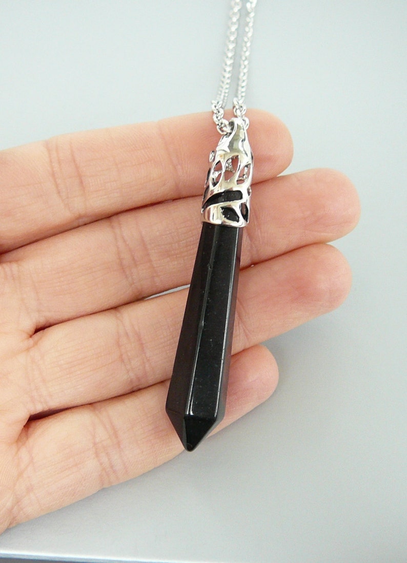 May include: A black gemstone pendant with a silver filigree design. The pendant is shaped like a long, pointed teardrop and hangs from a silver chain.