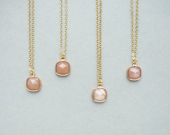 May include: Four gold necklaces with square-shaped pink sunstone pendants. The necklaces are on a light gray background.