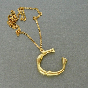 Può includere: Una collana con catena dorata con un grande ciondolo dorato a forma di lettera C astratta.