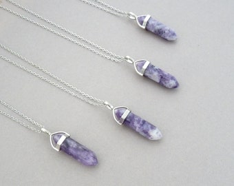 May include: Four silver necklaces with purple amethyst crystal point pendants. The necklaces are layered on a light gray surface.