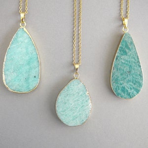 May include: Three teardrop-shaped amazonite pendants suspended from thin gold-toned metal chains. Each gemstone features a textured, mottled teal and light green surface with a polished gold-colored metal edge framing the irregular stone shape.