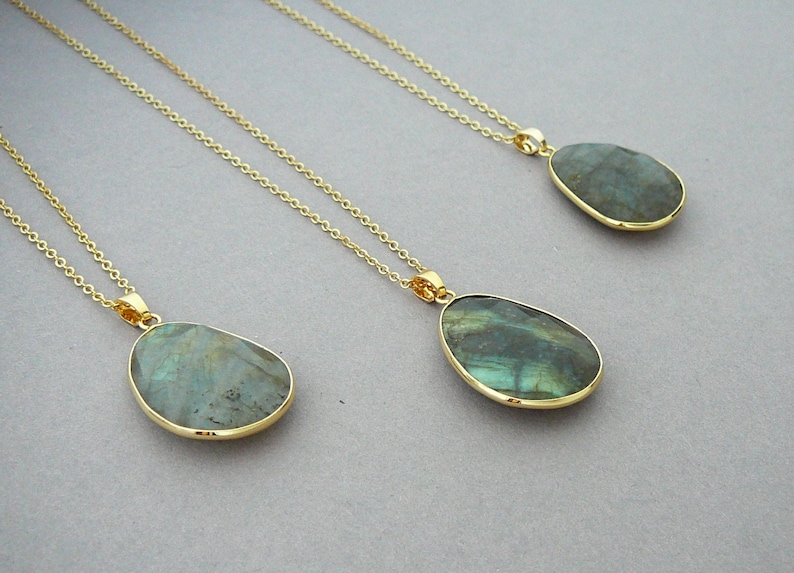 May include: Three gold necklaces with teardrop-shaped pendants. Each pendant features a polished, iridescent stone in shades of blue and green. The pendants are set in gold bezels and hang from delicate gold chains.