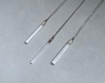 May include: Three silver necklaces with white crystal pendants. The pendants are long and rectangular.