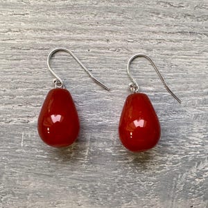 Puede incluir: Un par de pendientes de plata con piedras rojas en forma de lágrima.