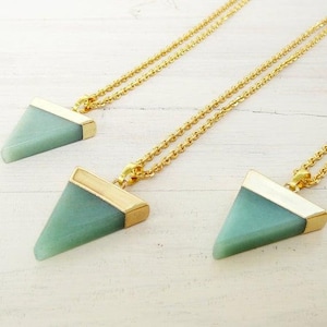 May include: Three gold necklaces with triangular green stone pendants. The pendants have a gold trim around the edges.