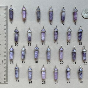 Puede incluir: Una colecci&oacute;n de veintiocho colgantes de cristal morado en forma de punta con engastes plateados, numerados del uno al veintiocho. Una regla en cent&iacute;metros y una moneda sirven de referencia, indicando una longitud de 3,8 cm por pieza.