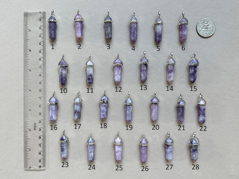 Puede incluir: Una colecci&oacute;n de veintiocho colgantes de cristal morado en forma de punta con engastes plateados, numerados del uno al veintiocho. Una regla en cent&iacute;metros y una moneda sirven de referencia, indicando una longitud de 3,8 cm por pieza.