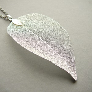 Op de afbeelding: Een zilveren blad hanger ketting met een delicaat, ingewikkeld ontwerp. Het blad is doorschijnend en heeft een subtiele glans.