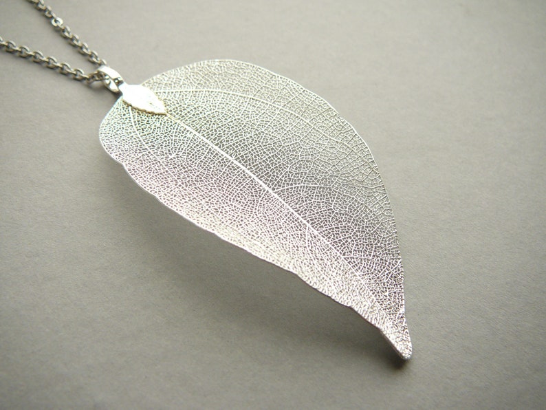 Op de afbeelding: Een zilveren blad hanger ketting met een delicaat, ingewikkeld ontwerp. Het blad is doorschijnend en heeft een subtiele glans.