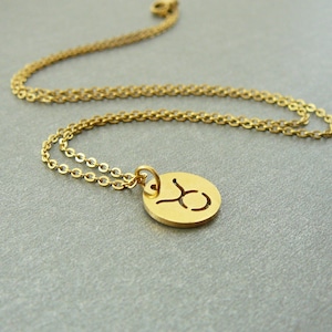 May include: Gold chain necklace with a round pendant featuring the Taurus zodiac symbol.