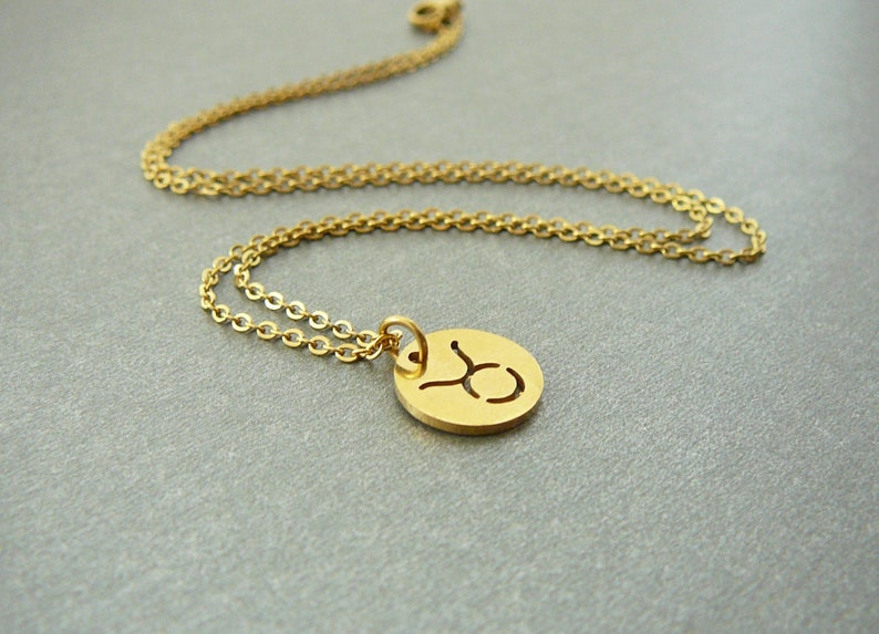 May include: Gold chain necklace with a round pendant featuring the Taurus zodiac symbol.