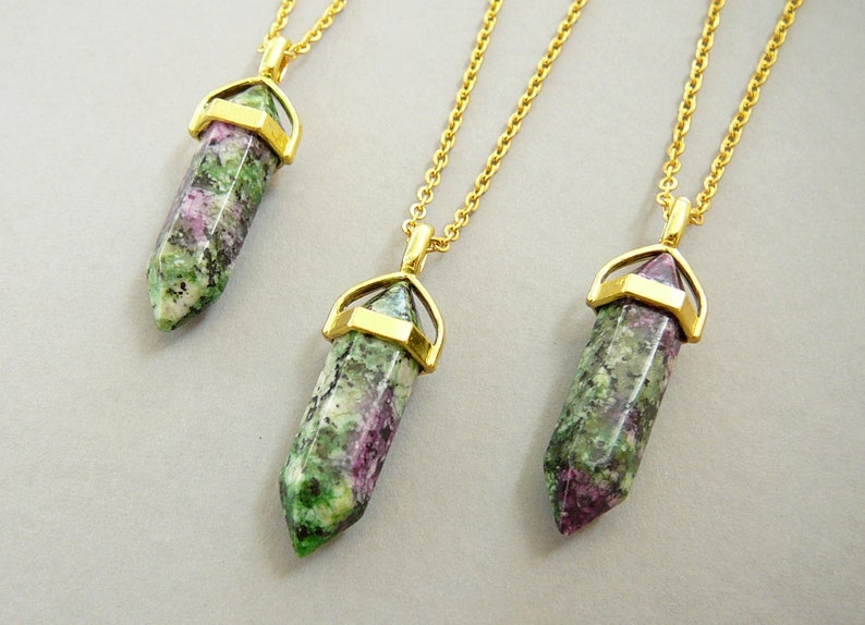 May include: Three gold necklaces with green and pink gemstone pendants. Each pendant is a pointed crystal shape with a gold setting.
