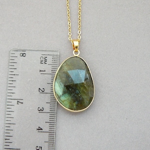 May include: A gold-colored necklace with a large, irregularly shaped pendant. The pendant is a faceted, iridescent gemstone, approximately 1.5 inches long, with shades of green and blue. The chain is delicate and also gold-colored.