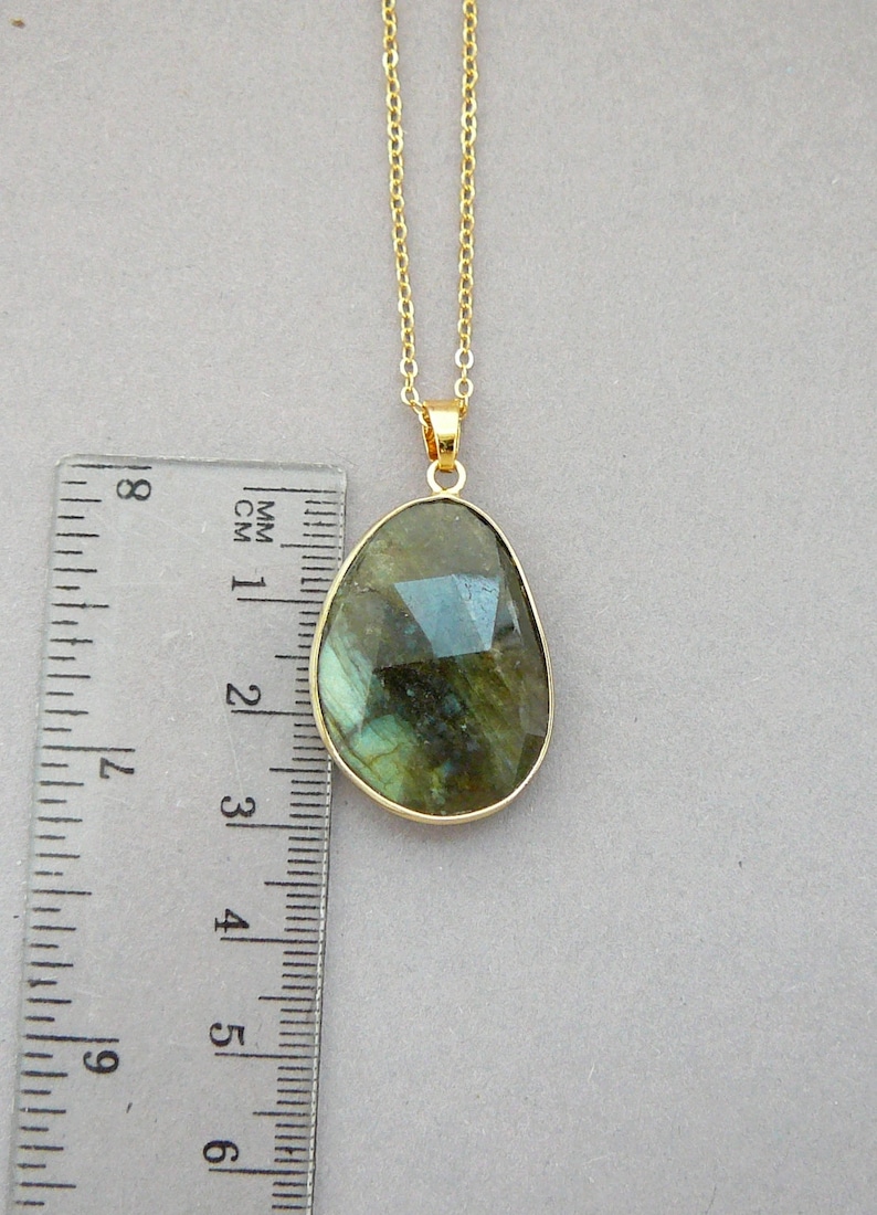May include: A gold-colored necklace with a large, irregularly shaped pendant. The pendant is a faceted, iridescent gemstone, approximately 1.5 inches long, with shades of green and blue. The chain is delicate and also gold-colored.