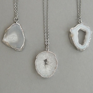May include: Three silver necklaces with white agate pendant charms. The pendants are all different shapes and sizes, with some having a hole in the center.