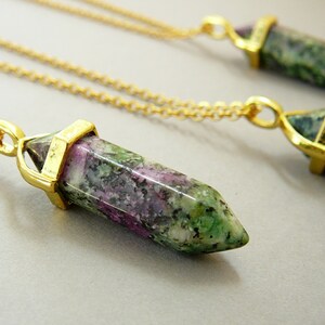 May include: Three gold necklaces with green, pink, and white gemstone pendants in the shape of a point. The pendants are attached to gold chains.