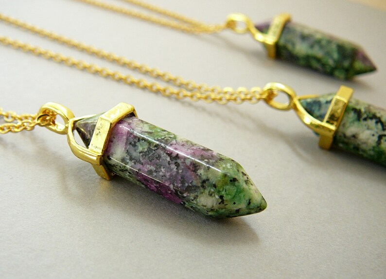 May include: Three gold necklaces with green, pink, and white gemstone pendants in the shape of a point. The pendants are attached to gold chains.