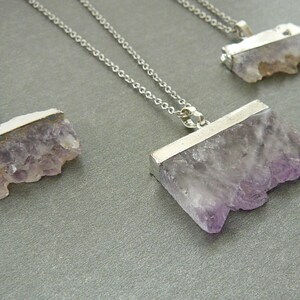 Pode incluir: Tr&ecirc;s colares com pingentes de cristal de ametista bruta de corte retangular e tampas de metal prateado. Cada pingente est&aacute; suspenso por uma delicada corrente prateada, exibindo os tons roxos naturais e a textura cristalina das pedras.