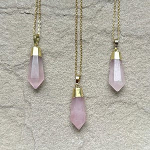 May include: Three gold necklaces with pink crystal point pendants. The pendants are faceted and have a gold setting.