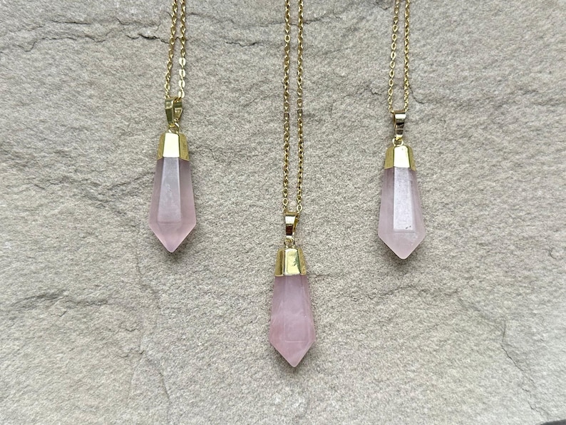 May include: Three gold necklaces with pink crystal point pendants. The pendants are faceted and have a gold setting.