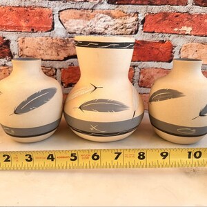 May include: Three ceramic vases with a beige background and gray and black feather designs. The vases are sitting on a white surface with a yellow measuring tape.