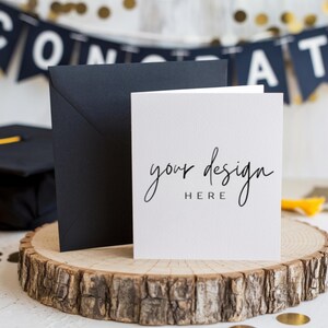 Peut inclure: Une carte blanche avec le texte "your design here" sur une tranche de bois. La carte est posée sur une enveloppe noire. Il y a des confettis dorés et un chapeau de graduation noir en arrière-plan.