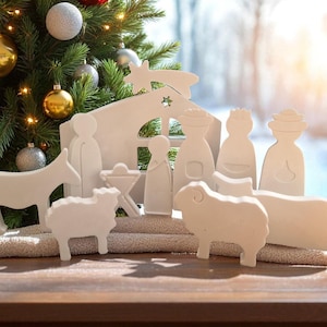 Peut inclure: Une crèche en bois blanc avec des figurines de la Sainte Famille, des rois mages et des animaux. La scène est posée sur une surface en bois avec un sapin de Noël décoré de boules en arrière-plan. Une décoration de vacances festive.