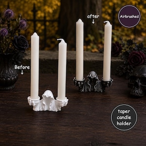 May include: Two taper candle holders shaped like hooded figures, each holding two white candles. One holder is solid white labeled 'Before', and the other is dark grey with airbrushed details labeled 'after'. The text 'Airbrushed' and 'taper candle holder' appear.