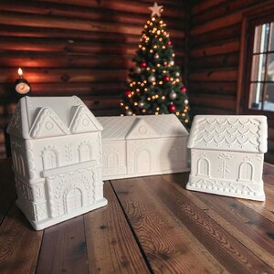 May include: Three white ceramic house-shaped containers with embossed architectural details including arched windows, doors, and textured roof patterns. The structures feature intricate relief designs on the exterior walls and roofs, presented as a set of decorative tabletop items.