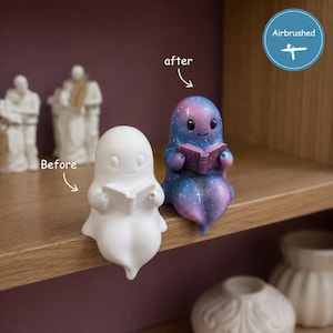 May include: Two ghost figurines are shown, one plain white and one airbrushed with a purple and blue galaxy pattern. Both ghosts are sitting and holding an open book. The text labels 'Before' and 'after' point to each figure, with 'Airbrushed' in a circle.