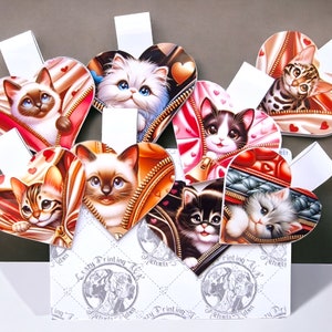 May include: A set of eight heart-shaped bookmarks featuring adorable kittens peeking out of zippered pouches. Each bookmark is decorated with a different kitten and a red, white, and gold color scheme. The bookmarks are arranged in a heart shape and are displayed on a white background with the text "Crazy Printing Tilda" repeated around the edges.