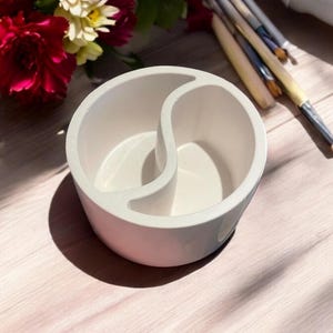 May include: White ceramic organiser with two divided compartments shaped like a yin yang symbol. The organiser is ideal for storing small items like brushes, pens, or pencils.