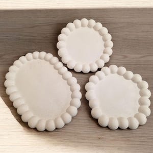 May include: Three white ceramic trays with a raised, textured rim. The trays are round and oval in shape.